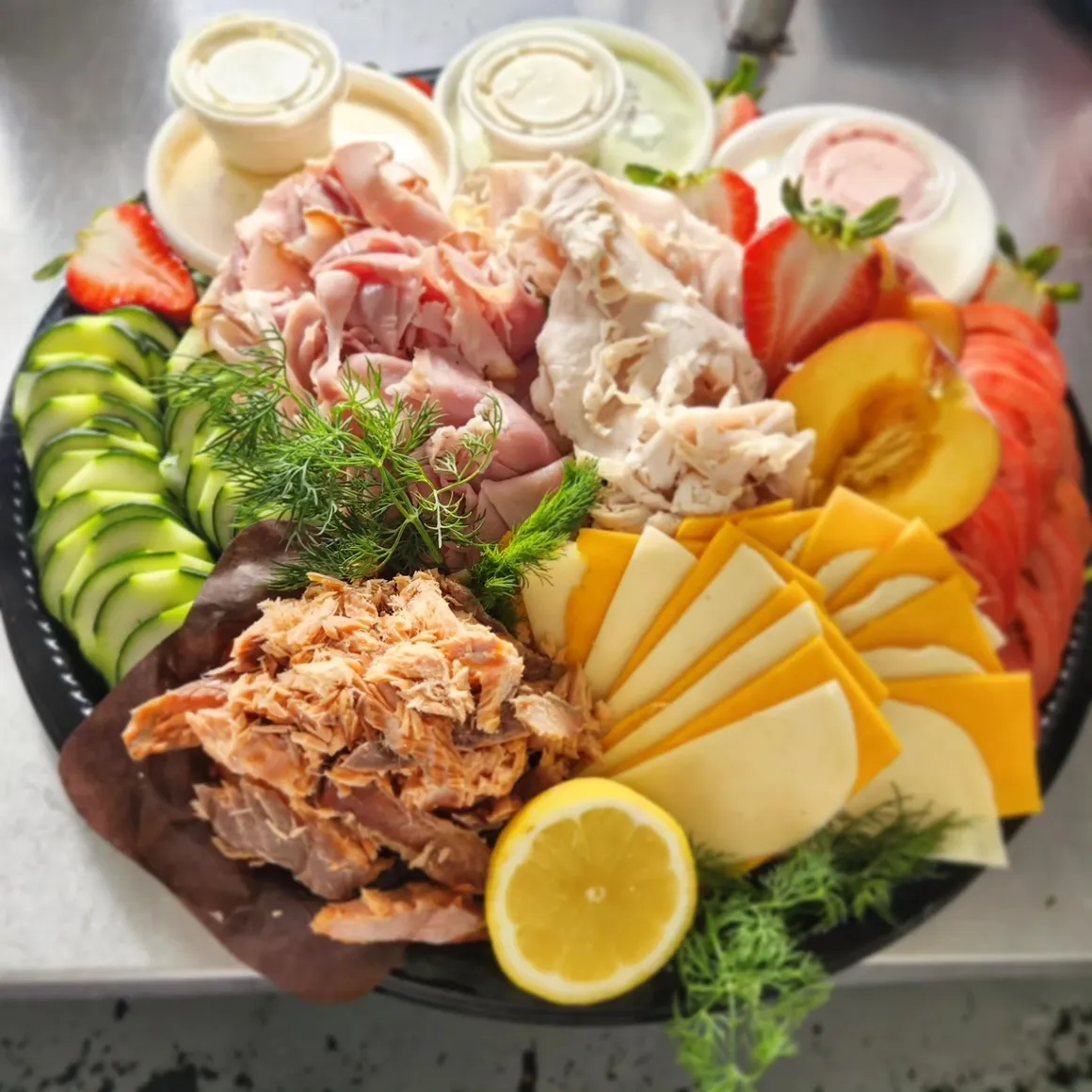 Brunch board from above — sliced meats, cheese fan, cucumber and dips